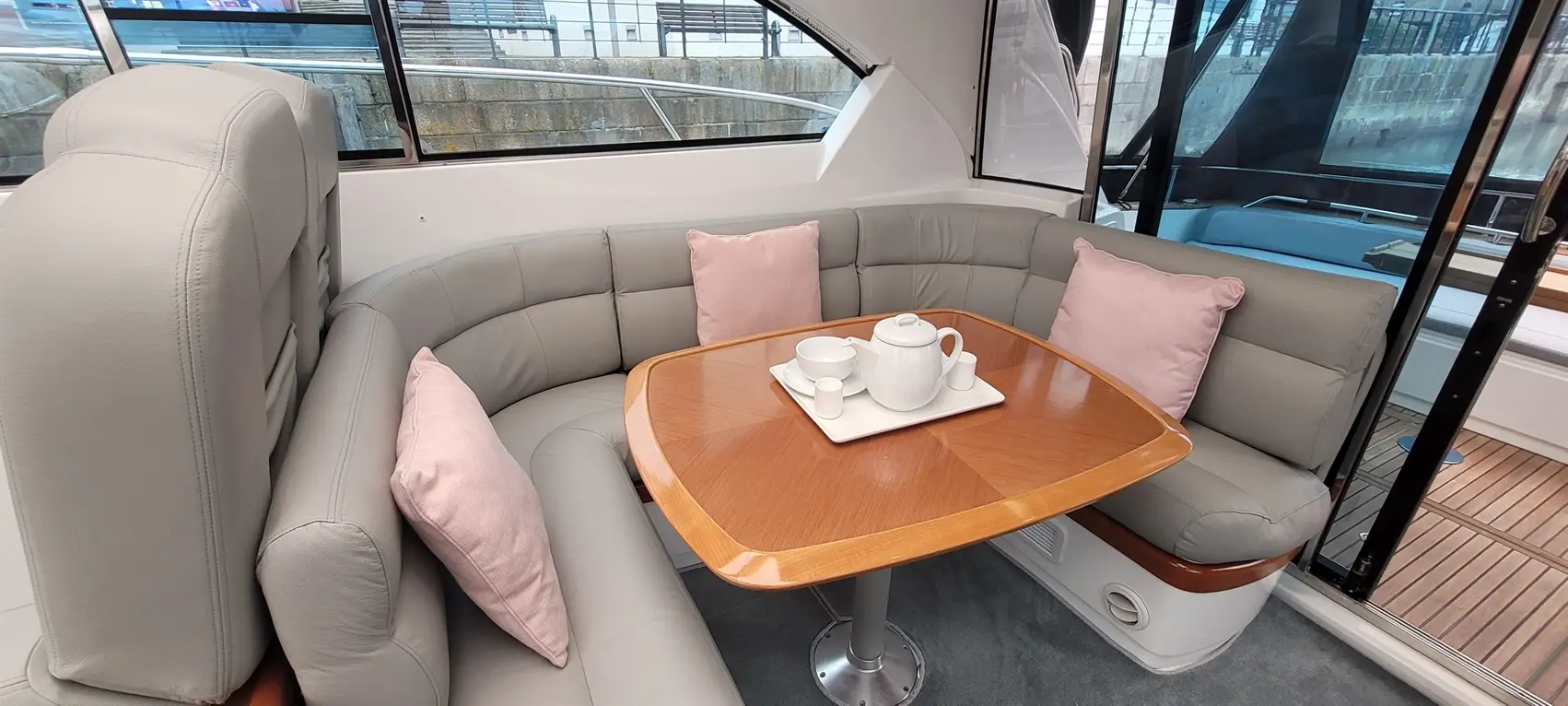 Cosy boat interior featuring a curved leather sofa with pink cushions, a wooden table set with tea pot and cups.